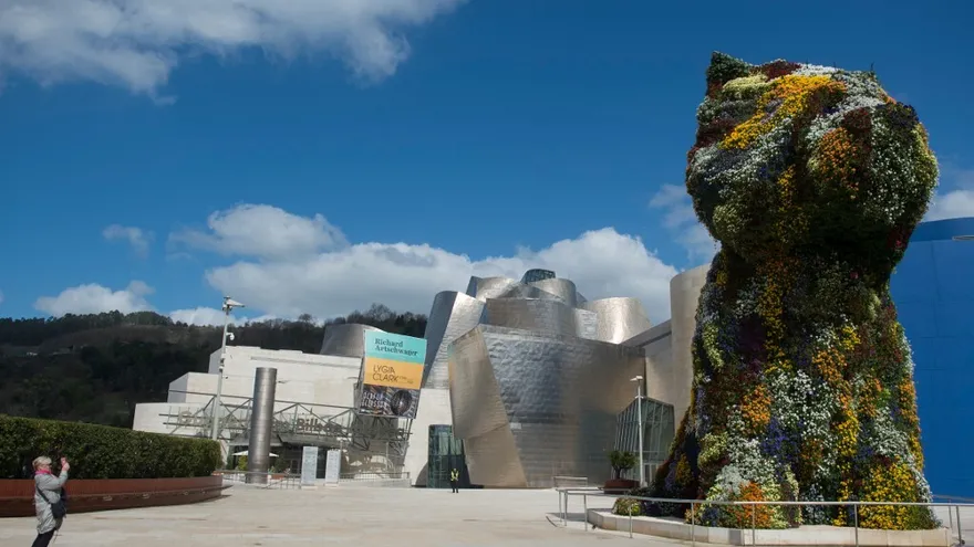 Una mujer toma una foto de la escultura en la parte de afuera de un  Museo Guggenheim de Bilbao totalmente libre de aglomeraciones debido a las restricciones del Coronavirus.