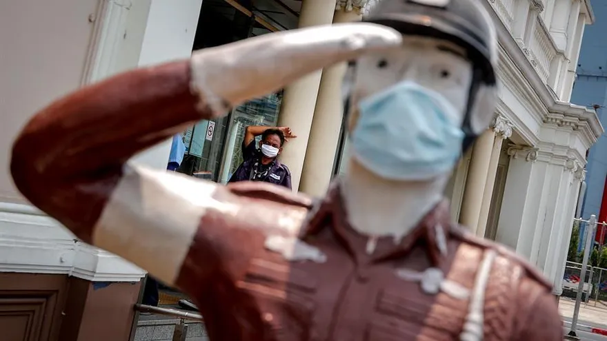 Un conductor de tuk tuk tailandés espera a los clientes detrás de una figura de un agente de policía protegido con una mascarilla este viernes 3 de abril en Bangkok, Tailandia.