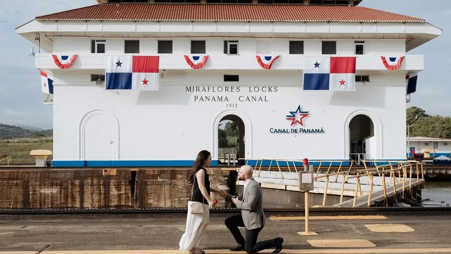 El diputado Broce se agacha y entrega el anillo en la pedida de matrimonio a su novia, con las esclusas de Miraflores al fondo