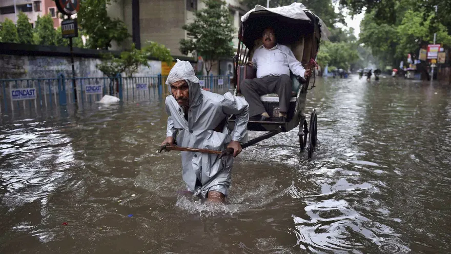 Un hombre transporta a un cliente en un carrito por una calle inundada tras las intensas lluvias caídas en Kolkata, India.