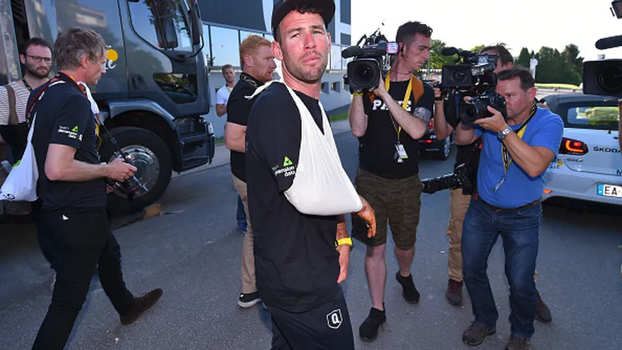 Mark Cavendish camina con un cabestrillo en su brazo mientras los camarógrafos lo siguen