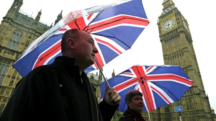 Peatones se protegen de la lluvia con paraguas mientras pasean frente al Palacio de Westminster, sede del Parlamento británico