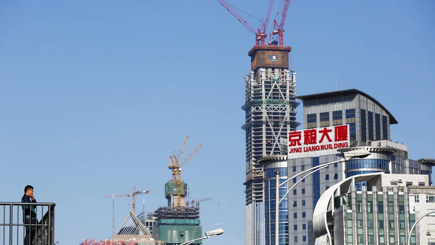 Un hombre fuma en un paso elevado junto a varios edificios en construcción en el Distrito Central Financiero de Pekín (China).