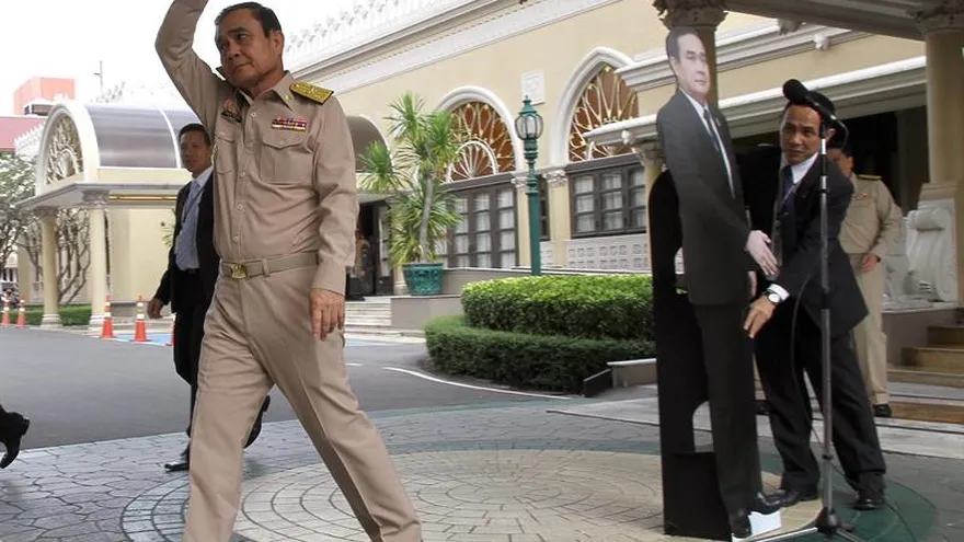 El primer ministro de Tailandia, Prayut Chan-o-cha, se despide de los periodistas con la seña "te quiero" del lenguaje de signos mientras deja una fotografía suya a tamaño real ante el micrófono en Bangkok.