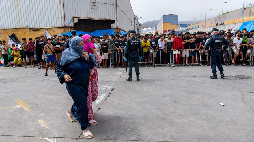 Agentes de la Policía Nacional de España permanecen en el lugar mientras migrantes esperan durante una distribución de alimentos