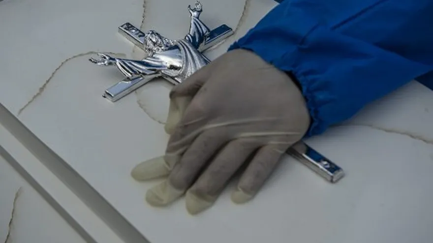 Una persona toca el féretro de un familiar fallecido por COVID-19