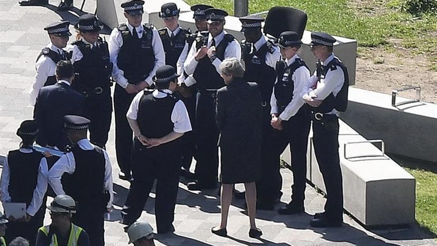 La primera ministra británica, Theresa May (c), conversa con agentes de la policía británica en el lugar donde se originó el miércoles el devastador incendio en una torre residencial de Londres, Reino Unido, hoy, 15 de junio de 2017.