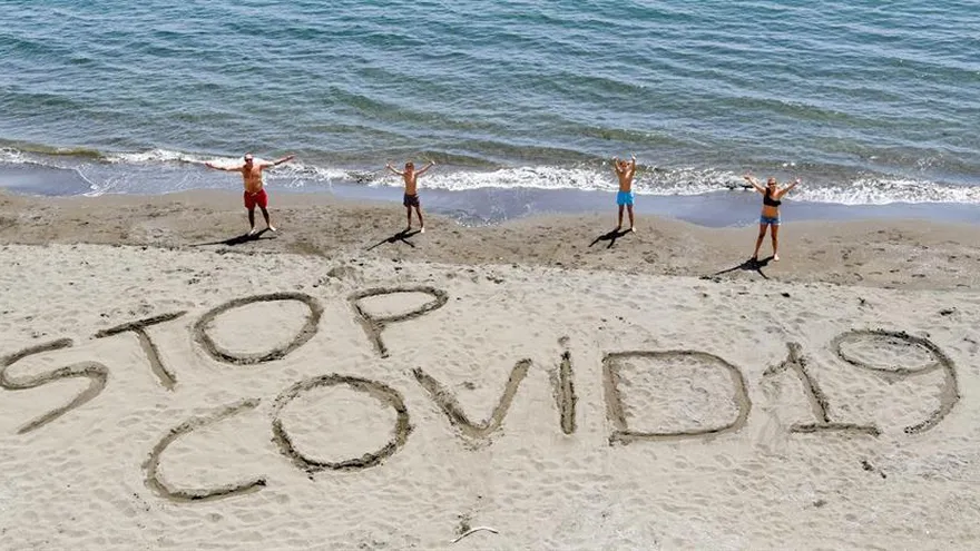 Una familia escribe la frase "Stop Covid-19" en la arena de una playa de Nápoles, Italia, este sábado.