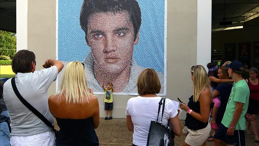 Seguidores de Elvis Presley se toman fotos frente a un afiche en la calle en Graceland, el hogar del cantante y actor estadounidense en Memphis, Tennessee.
