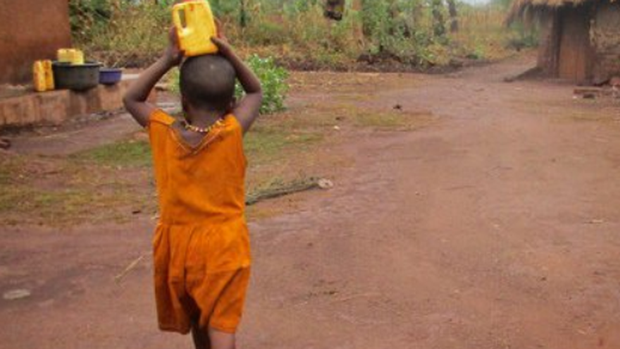 Un niño transporta sobre su cabeza una botella con agua