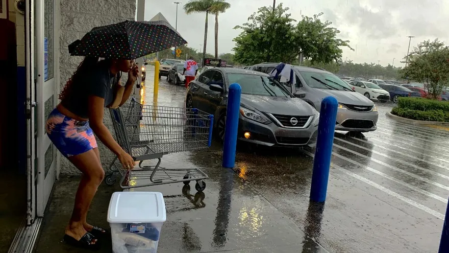 Una mujer se protege con un paraguas en la entrada de un establecimiento comercial en Fort Lauderdale mientras la ciudad de prepara para recibir al huracán Dorian.