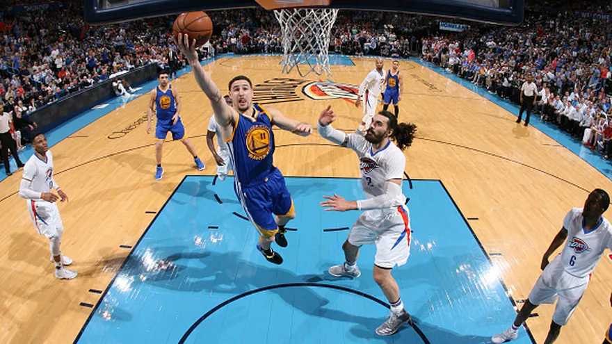 Klay Thompson (i) salta hacia la canasta ante la cobertura de Steven Adams (d)