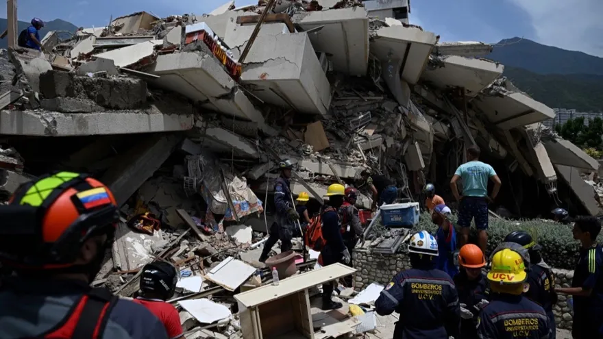 Firefighters and rescuers stand next to a collapsed building following a twin earthquake in Los Corales, La Guaira