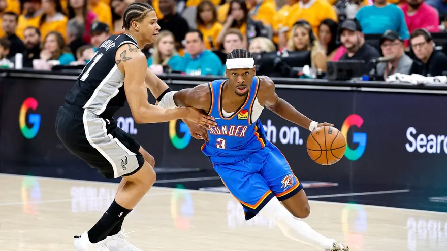 Shai Gilgeous-Alexander (d) intenta evadir la cobertura de Carter Bryant (i)