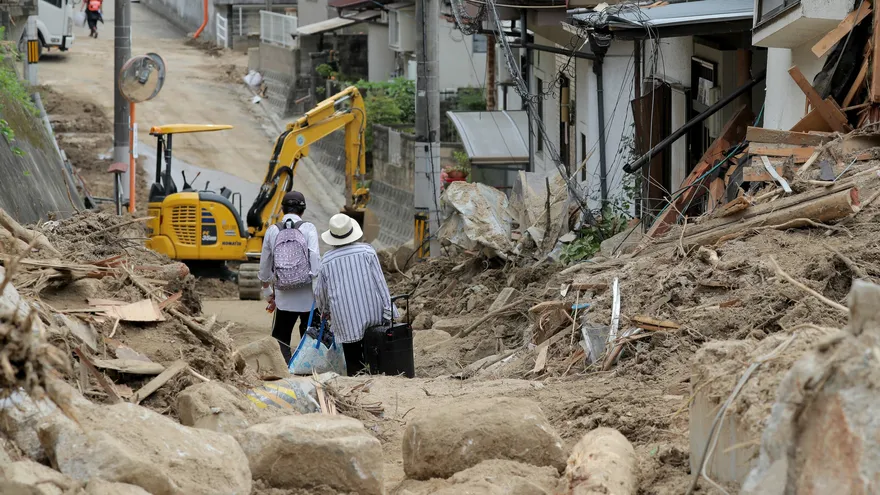 Dos ancianos cargan con sus pertenencias por una zona arrasada por las inundaciones de camino a un centro de alojamiento temporal en Hiroshima (Japón)