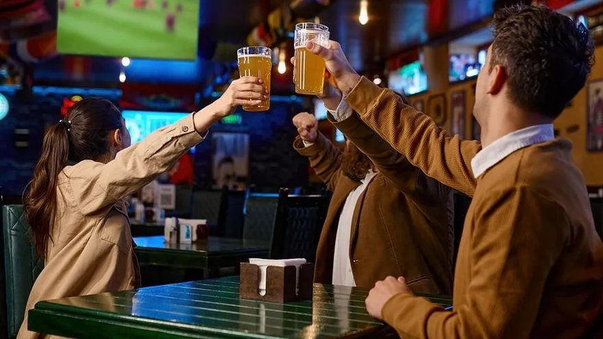 Un grupo de personas brindan con cervezas en un bar.