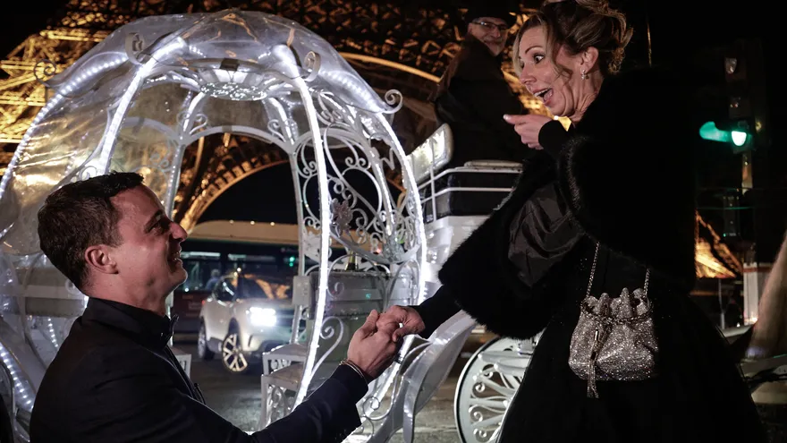 Un hombre pide la mano a su novia y de fondo una carroza cerca de la Torre Eiffel
