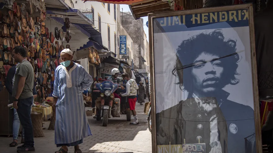 Personas compran en un mercado y cerca se observa un retraro de Jimi Hendrix
