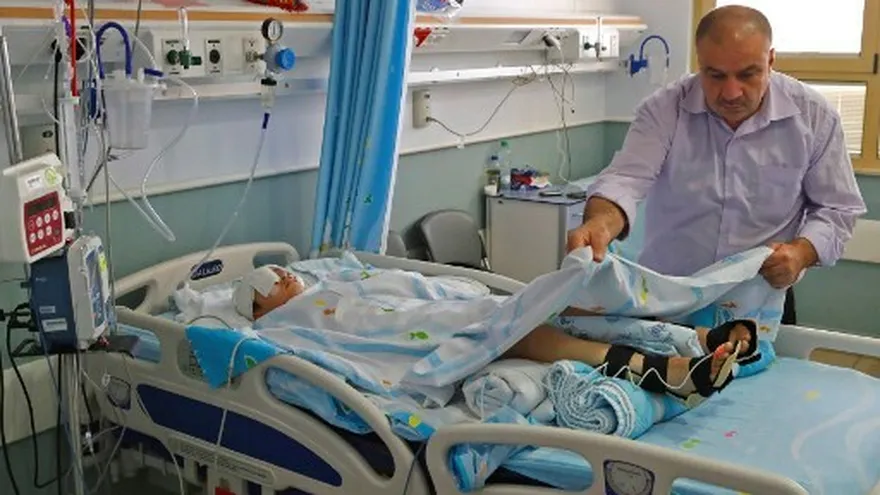 El palestino Yasser Shtewi cuidando a su hijo Abdelrahman, mientras yace en una cama hace casi un mes en el Hospital Sheba en Ramat Gan, cerca de la costa israelí de Tel Aviv.