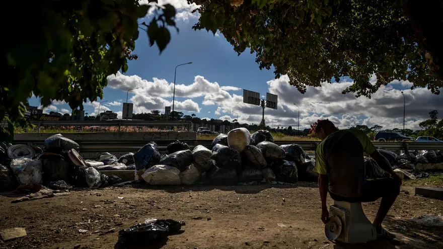 Fotografía del pasado 22 de diciembre de un hombre sentado cerca de desperdicios reciclados sobre un puente en la ciudad de Caracas (Venezuela)