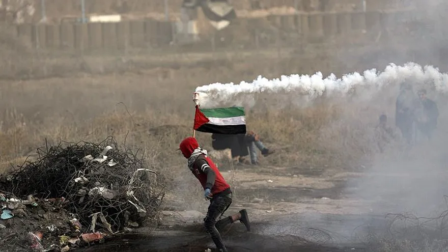 Un joven palestino sostiene una granada de gas lacrimógeno lanzada por miembros del ejército israelí, ayudándose de una bandera de Palestina, cerca de la frontera de Gaza con Israel, durante los enfrentamientos.