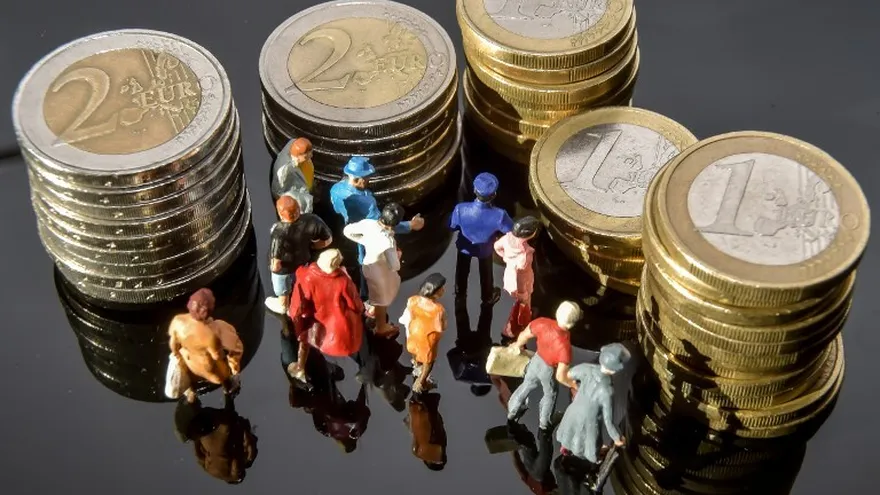 Foto ilustrativa: Diminutas figuras de personas rodean monedas de 1 y 2 euros