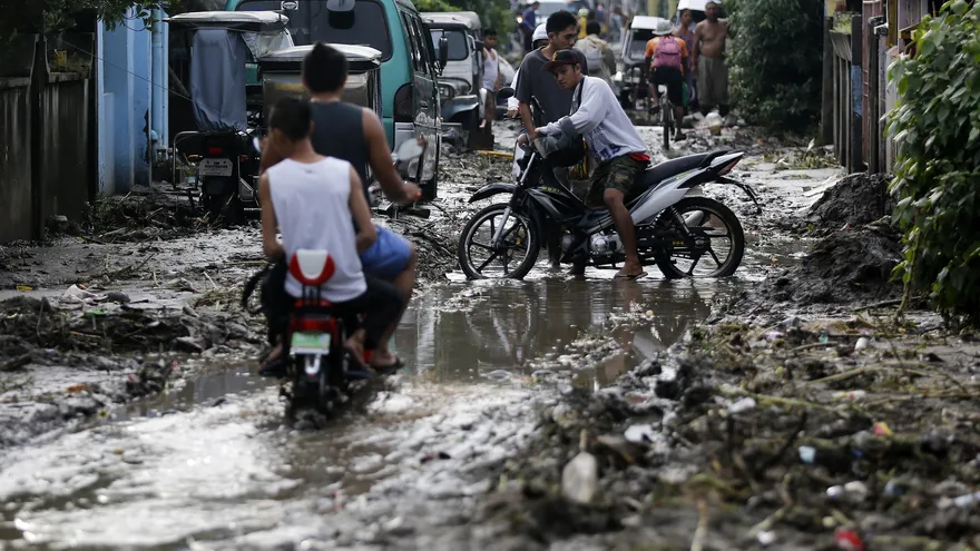 Filipinos transitan por una vía inundada y cubierta de lodo, en Noveleta, Cavite (Filipinas