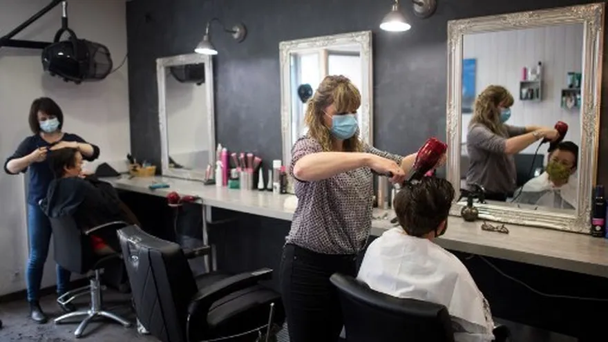 Personas en un salón de belleza donde se observan medidas de distanciamiento social y uso de mascarillas