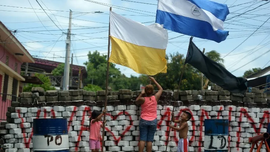 Foto archivo. Una mujer y niños colocan una bandera de Nicaragua, el Vaticano y negra en una barricada en el barrio de Monimbo en Masaya.