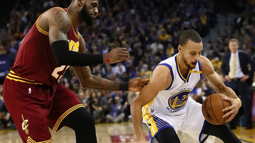 Stephen Curry (d) conduce el balón ante la marca de LeBron James (i)