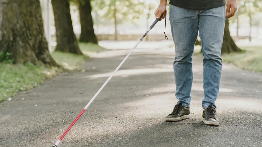 Un hombre con discapacidad visual camina por una calle apoyado de su bastón.