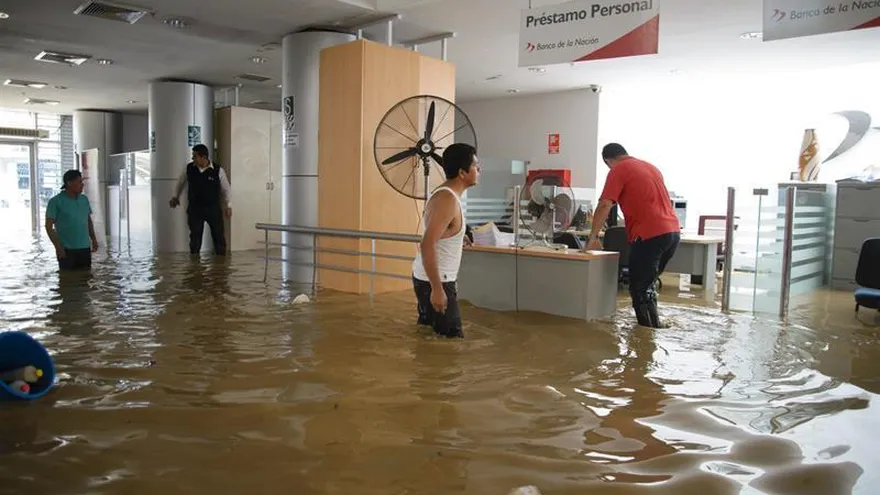 Un grupo de personas camina por una de las oficinas del banco de la Nación, inundada por el río Piura, este lunes 27 de marzo de 2017, en Piura (Perú).